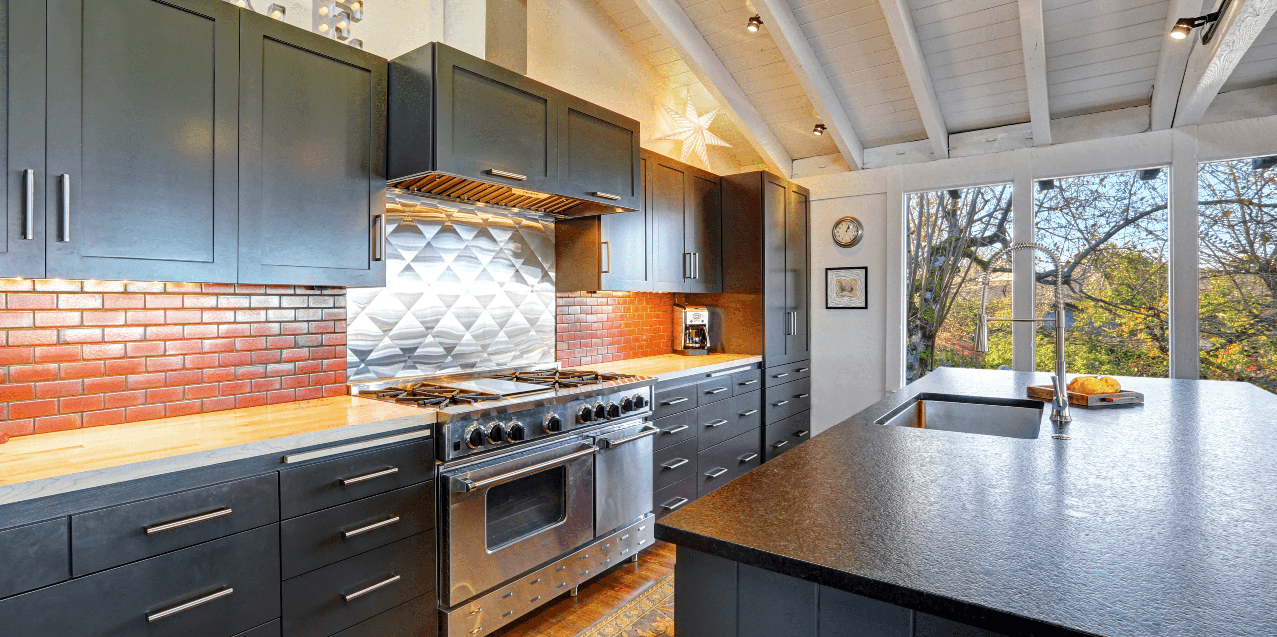 Modern kitchen featuring sleek black cabinetry, stainless steel appliances, and a textured backsplash, with large windows offering a view of nature.