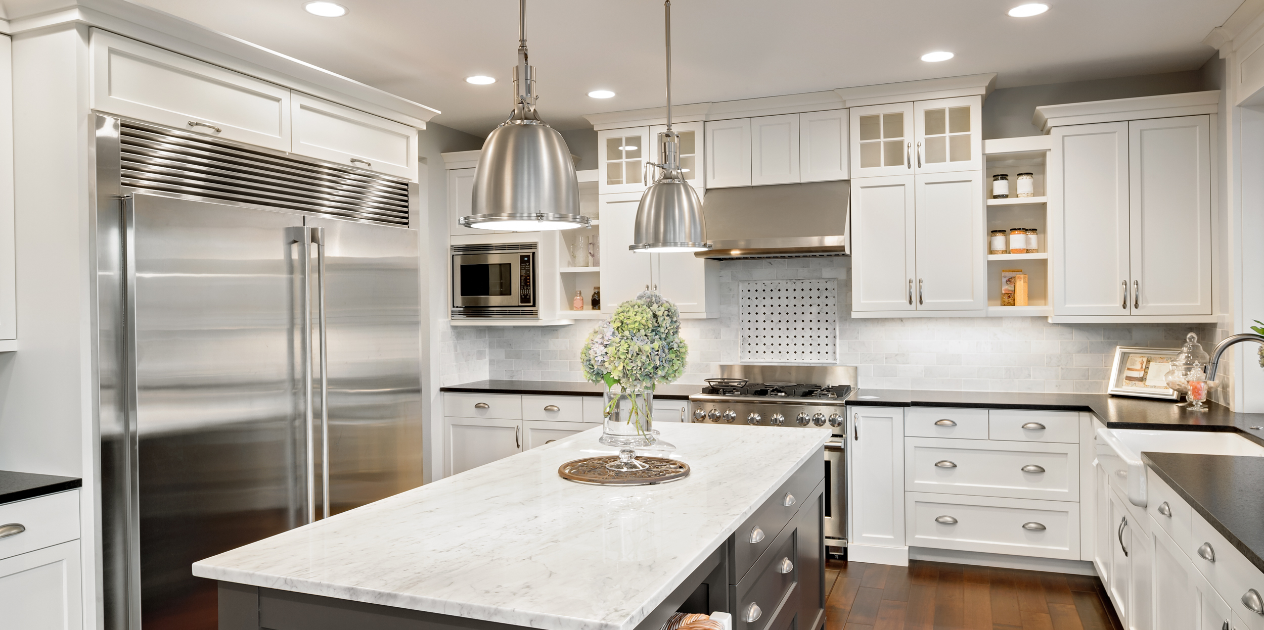 Modern kitchen featuring stainless steel appliances, a marble-topped island with a floral centerpiece, and white cabinetry for a sleek appearance.