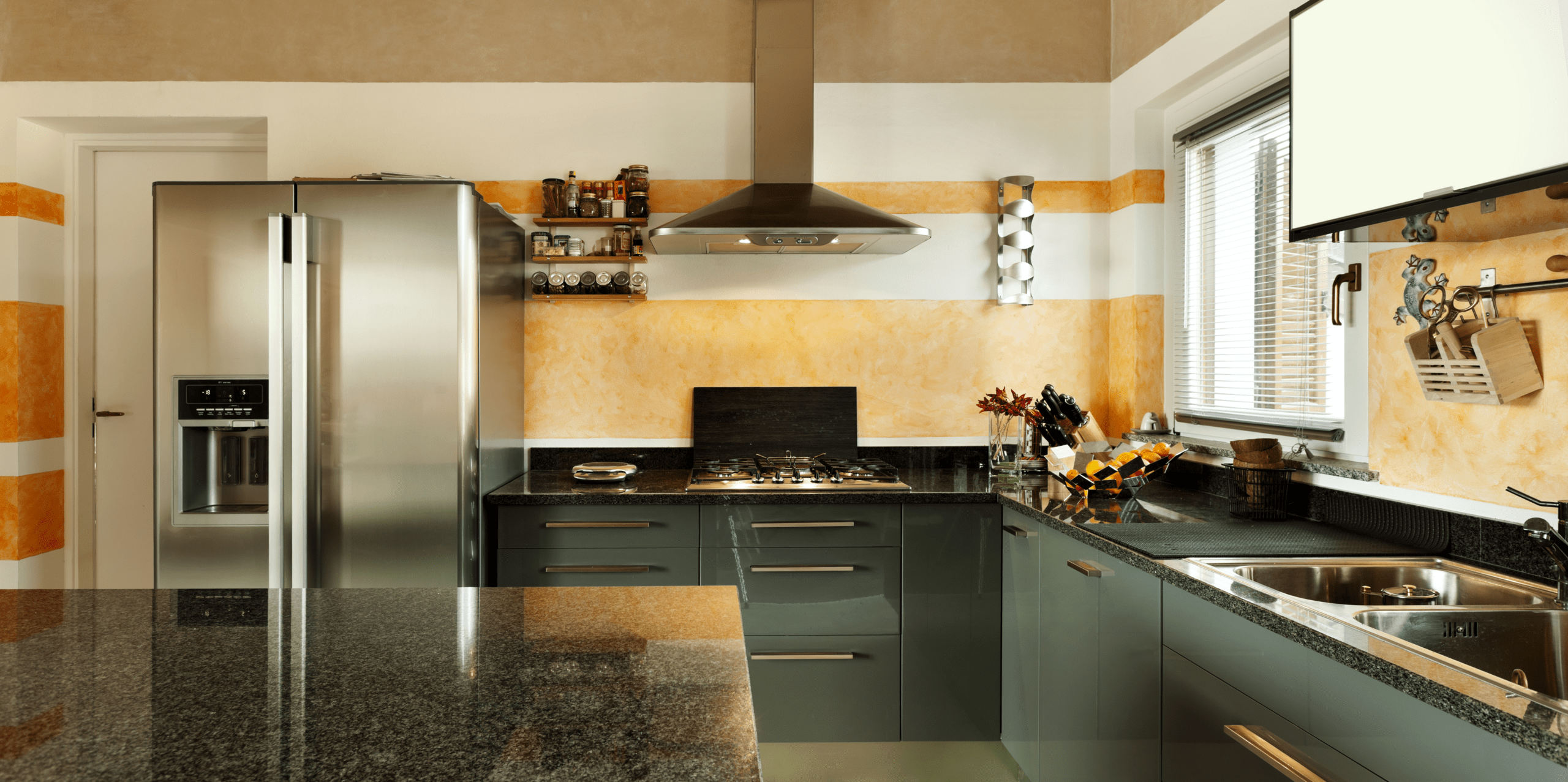 Modern kitchen featuring sleek gray cabinetry, a stainless steel fridge, gas stove, and decorative orange accents on the walls.